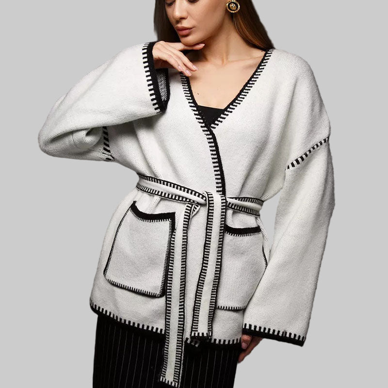 Woman wearing a white cardigan with black trim on a dark background